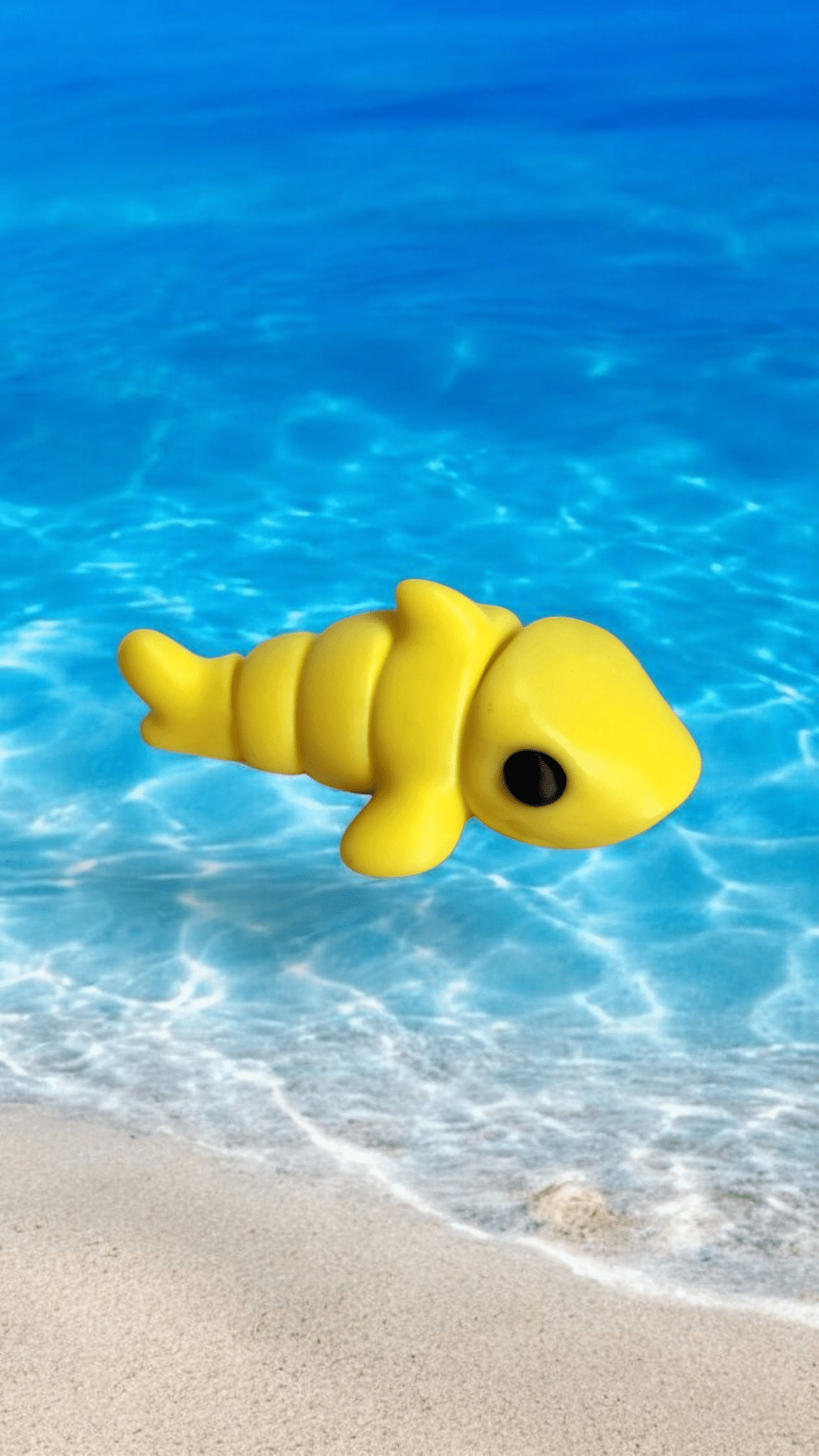 A toy yellow shark floating in the ocean near the edge of the beach.