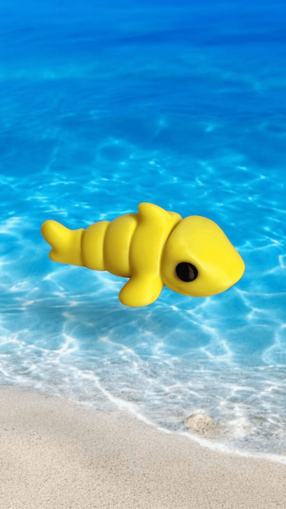 A toy yellow shark floating in the ocean near the edge of the beach.